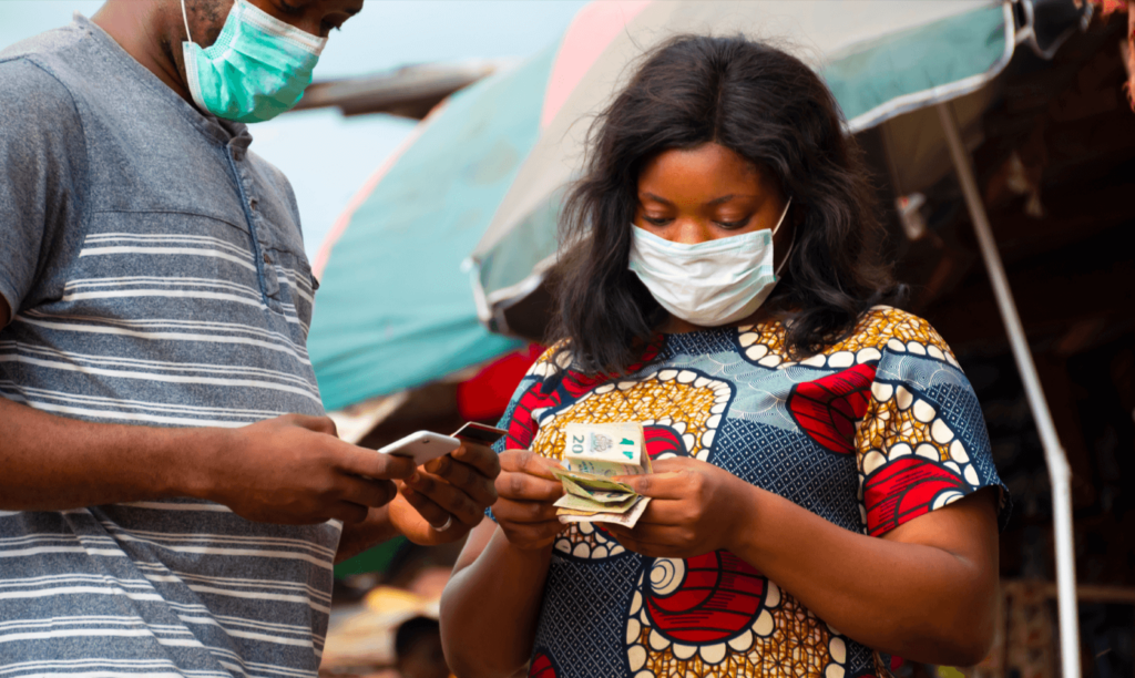 People with masks on, one holds a phone while the other holds money