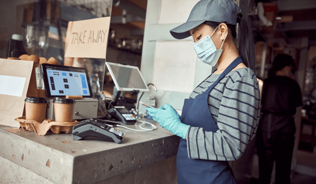 Person working cash register while wearing protective COVID gear