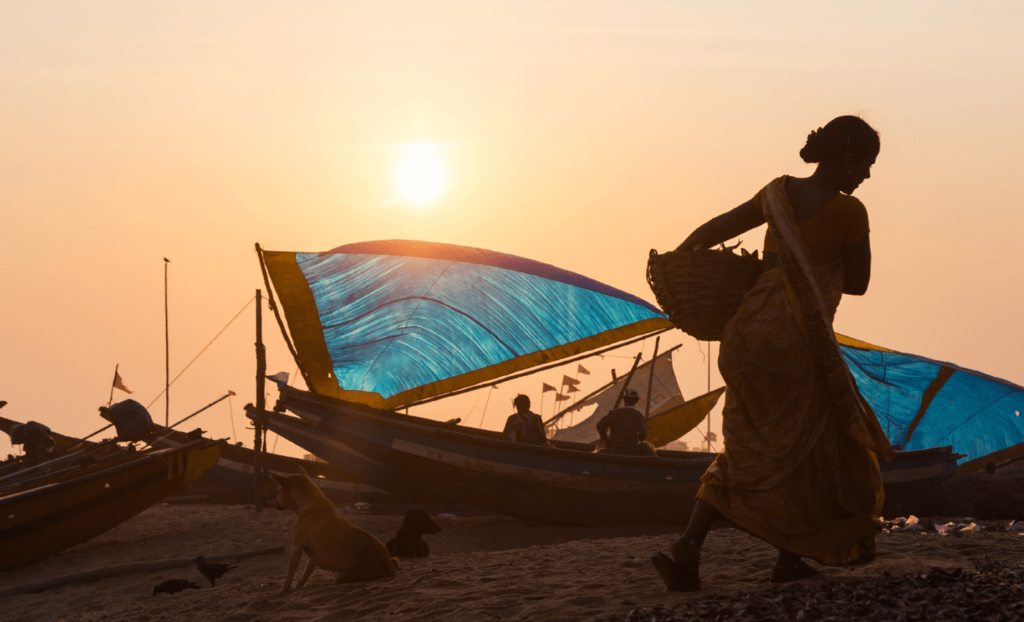 People and boats on a beach while the sun sets